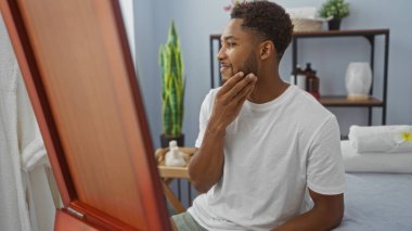 Güzellik ürünleri ve sağlık dekorlarıyla çevrili, aynada yüzünü inceleyen yakışıklı bir adam.