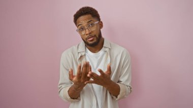 Soyutlanmış pembe arka plan duvarını aşan yakışıklı genç adam şaşkın görünüyor.