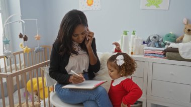 Bir kadın telefonda konuşurken birden fazla iş yapıyor ve dikkatli kızı yakınlardayken notlar yazıyor. Oyuncak ve bebek bakımı gereksinimleriyle dolu sıcak, kapalı bir aile ortamını yansıtıyor..