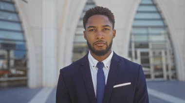 Takım elbiseli yakışıklı Afro-Amerikan bir adam şehirdeki bir sokak ortamında güvenle ayakta duruyor.