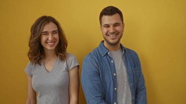 Gülümseyen adam ve kadın, sarı bir arka plana karşı birlikte, neşeli ve rahat bir ortamda mutlu ilişkilerini ve parlak ifadelerini sergiliyorlar..