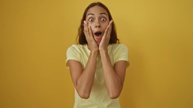 İzole edilmiş sarı arka plan duvarında şaşırdığını ifade eden genç bir kadın.