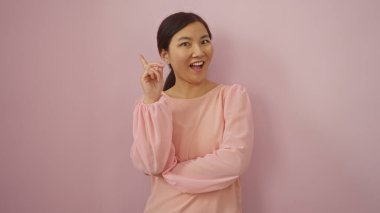 Pembe arka planda gülümseyen bir kadın fikir jesti yapıyor, yaratıcılık ve ilham taşıyor, tecrit edilmiş genç Çinli bir yetişkin düşünceli bir ifade sergiliyor, yenilik öneriyor..