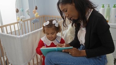Anne ve kızı yatak odasında beşiğiyle birlikte yazışıyorlar, sıcak bir yuva ortamında aile sevgisi ve bağlantı anlarını yakalıyorlar..