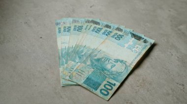 Para birimi tasarımının detaylarını gösteren somut bir yüzey üzerine 100 reais 'lik Brezilya banknotları sergilendi.