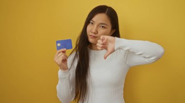Sarı arka planda kredi kartı tutan Asyalı kadın onaylamadığını belirtiyor..