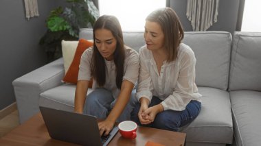 Anne ve kızı birlikte oturma odasında oturuyorlar, bir sehpanın üzerinde dizüstü bilgisayar kullanıyorlar ve ortak aktiviteleri paylaşıyorlar.