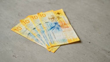 İsviçre 'nin on franklık banknotları beton bir yüzeyde yer alır, parlak sarı ve mavi renkler ayrıntılı tasarımlarla gösterilir, İsviçre' nin para birimini temsil eder..