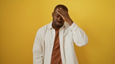 Yakışıklı, Afro-Amerikalı bir adam izole edilmiş sarı arka plana karşı düşünceli ve endişeli görünüyor.