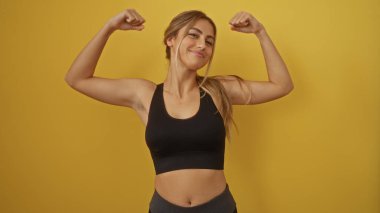 Atletik bluz giymiş bir kadın izole edilmiş sarı arka plana karşı kas gücü, sağlıklı yaşam tarzı ve kendine güveni sergiliyor pozitiflik ve güç yayıyor..
