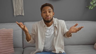 Şaşkın suratlı genç bir adam şık bir oturma odasında oturmuş, modern dekorla rahat bir atmosfer yayıyor..