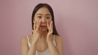 Çin 'den gelen Asyalı bir kadın pembe bir arka plan üzerinde yanaklarına dokunuyor, güzel ve çekici bir hava yayıyor..