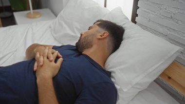 İspanyol bir adam rahat bir yatak odasında rahat bir yatakta huzur içinde dinleniyor. Huzurlu bir evde rahatlık ve sükunet gösteriyor..