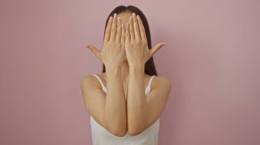 Yüzünü pembe bir duvara yaslayan, beyaz bir üst giysili, izole bir arka planı olan bir kadın..