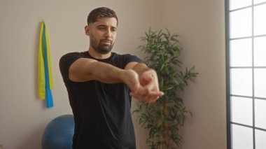 Spor salonunda arka planda spor malzemeleriyle esneyen genç bir adam sağlık ve zindeliğe odaklanıyor..