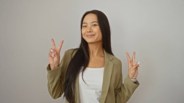Güzel genç Çinli kadın gülümsüyor ve iki eliyle izole edilmiş beyaz arka planda barış işaretleri yapıyor.