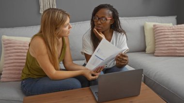 Oturma odasında dizüstü bilgisayarla dokümanları tartışan kadınlar, kapalı bir ortamda profesyonel bir sohbetin altını çiziyor