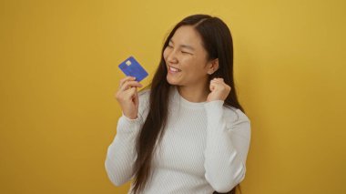 Sarı arka planda kredi kartı tutan gülümseyen bir kadın mali başarı ve kredi güveninin neşe ve memnuniyetini gösteriyor.