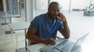 Telefondaki genç adam ofiste dizüstü bilgisayar kullanıyor.