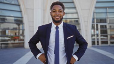 Takım elbiseli yakışıklı Afrikalı bir adam şehrin sokak ortamında güvenle ayakta duruyor.