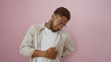 Gözlüklü yakışıklı genç adam izole edilmiş pembe bir arka planda acı içinde sırtını tutuyor.