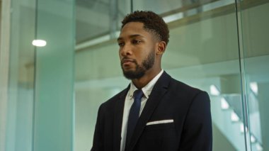 Takım elbiseli yakışıklı Afro-Amerikan bir adam modern bir ofiste duruyor ve işine odaklanıyor.