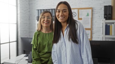 Parlak bir ofis ortamında gülümseyen kadınlar, çalışanların birlikte çalıştığı dostane ve profesyonel bir çalışma ortamı tasvir ediyorlar..