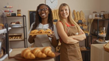 Kadın fırıncılar fırının iç kısımlarında taze hamur işleri sunmaktan gurur duyarlar, pişmiş yiyecekler ve dekoratif raflarla çevrili..
