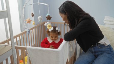 Sıcak bir evde kızıyla oynayan bir kadın, sıcak bir aile ortamında sevgi ve ilgi gösteriyor. Etrafında bir beşik ve oyuncaklar var..