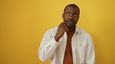 Beyaz gömlekli yakışıklı, Afro-Amerikan bir adam ve izole edilmiş sarı arka planda düşünceli bir poz.