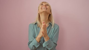 Orta yaşlı bir kadın, güzel gülüşünü ve sarı saçlarını gösteren pembe bir arka plana sevinçle alkışlar..