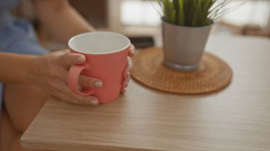 Kahve fincanı tutan bir kadın. Kapalı bir kafe ve ahşap bir masa üzerinde hasır bir bardak.