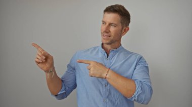 Mavi gömlekli bir adam, gri arka planda rahat ve modern tarzını sergiliyor. Kendine güvenen bir ifadeyle jest ve odaklanmayı vurguluyor..