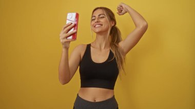 Kadın kendine güvenen akıllı telefonuyla canlı sarı arka planda poz veriyor. Rahatlamış selfie çekiminde güç ve güzellik sergiliyor. Neşeli anları yakalıyor..