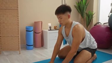 Huzurlu bir spa odasında yoga aksesuarlarıyla yoga minderinin üzerinde uzanan genç bir adam.