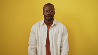 Afro-Amerikalı adam, sarı arka planda dikiliyor. Gömlek giyiyor ve küçük boy işareti ile işaret ediyor. Parmaklarını kullanıyor, ölçü ve önem kavramını vurguluyor.