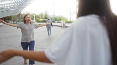Şehir parkında sevgi dolu bir şekilde kucaklaşan kadınlar, arkadaşlığı ve bağlantıyı kutluyor, dışarıdaki ilişkilerinin neşe ve sıcaklığını vurguluyor.
