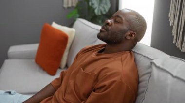 Genç adam rahat oturma odasında rahat yastıklar ve hafif ışıklandırmayla dinleniyor.