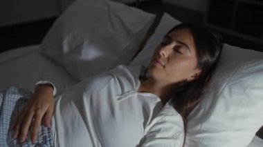 Bir kadın yatak odasında huzur içinde uyuyor, sakin ve huzurlu bir ortam sergiliyor..