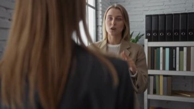 Kadınlar modern bir ofiste belgeler ve raflarla iş konuşuyorlar, profesyonelliği ve iyi aydınlatılmış bir kurumsal ortamda takım çalışmasını vurguluyorlar.