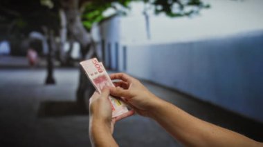 Bir şehir caddesinde İsveç kronu banknotları sayan bir adam, açık hava ortamında para ve yatırım temaları vurguluyor.