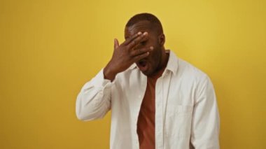 Afro-Amerikan bir adamın yüzü. Gömlek giyip ayakta dikiliyor, parmaklarının arasından bakıyor. Utanç dolu elleri örtüyor.