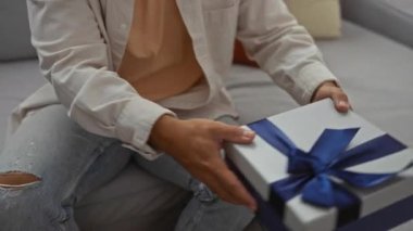 Erkekler oturma odasında birbirlerine hediye veriyorlar. Yumuşak ışıklandırmalı ve günlük kıyafetli rahat bir dairede yakın bir ilişki öneriyorlar.