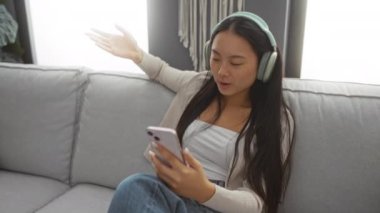 Evde dinlendirici bir iç mekanda kulaklıkla müzik dinleyen Asyalı kadın..