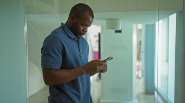 Ofisteki genç adam yüzünde bir gülümsemeyle akıllı bir telefon kullanarak iş yerinde çekici ve çekici bir an yaşatıyor.