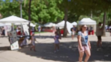 Açık hava pazarında, ağaçların altındaki tezgahlarda bokeh etkisi yaratan insanları bulanıklaştırdı.