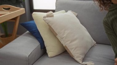 Yeşil kazaklı, kıvırcık saçlı, rahat bir atmosferi olan, apartman dairesindeki yastıklı, rahat bir kadın oturma odasında dinleniyor..