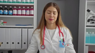 Klinikteki doktor, üniformalı beyaz bir kadın, mutlu ve gururlu bir ifadeyle kendini işaret ediyor.