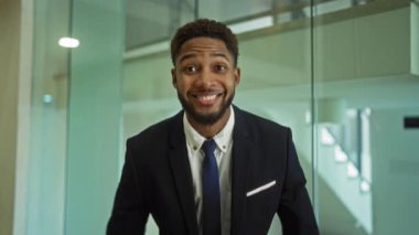 Ofiste gülümseyen genç bir adam. Başparmakları havada, takım elbiseli ve kravatlı. Kapalı alanda olumlu ve kendinden emin bir tavır sergiliyor.