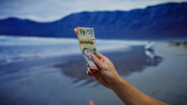 Manzaralı bir İzlanda plajında Avustralya doları tutan bir adamın elleri, finans unsurlarını birleştiriyor ve deniz kenarında eşsiz bir açık hava ortamında seyahat ediyor..